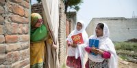 A woman opens the curtain to her home for Tayyaba Gul (right), of the Rotary Club of Islamabad (Metropolitan), and Parveen Ajmal, Lady Health Worker, who are there to talk to women with families during a door-to-door campaign in Nowshera, Pakistan. 04 August 2019. Building on Rotary's work with the global health community and its GPEI partners, Rotary members in Pakistan build relationships with families that are focused on health care. As part of their commitment to eradicate polio, Rotary clubs sponsor he